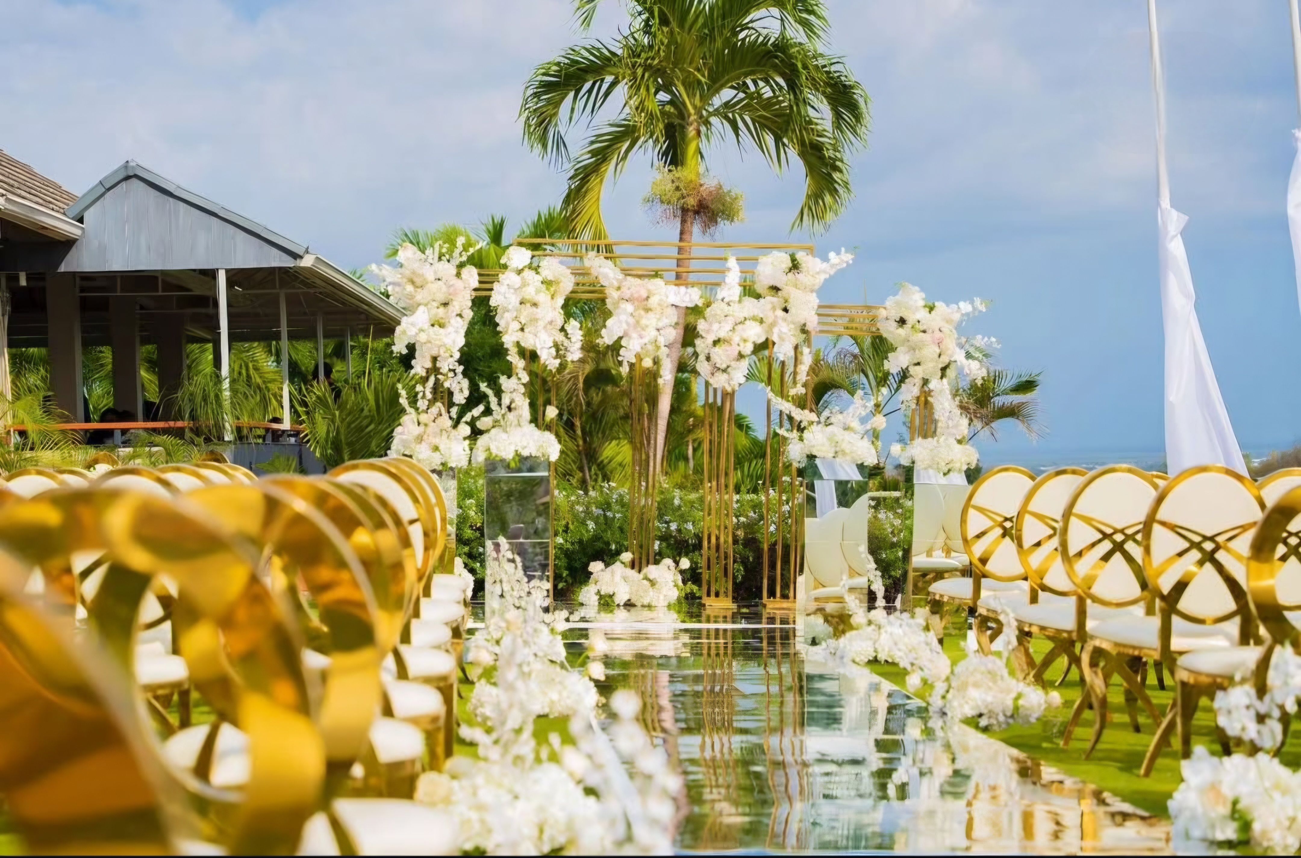 Outdoor ceremony aisle with white florals, gold chairs, and garden greenery